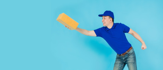 Asian happy delivery man wearing a blue shirt running and carrying paper parcel boxes isolated on on blue colour background with copy space.Concept of Postal delivery service.