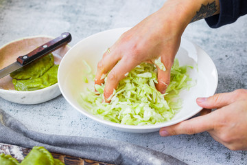 Woman crumples fresh grated cabbage with hands in bowl. Make detox vitamin salad. Vegan dieting food.