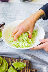 Woman crumples fresh grated cabbage with hands in bowl. Make detox vitamin salad. Vegan dieting food.