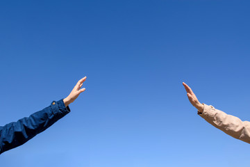 Two hands in a welcome gesture. Dark and light sleeve of clothes. Background blue sky. Concept of maintaining social distance in a pandemic of the covid-19 virus.