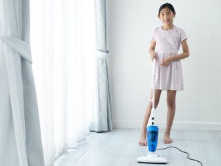 Asian girl using vacuum cleaner, girl standing near window at home during COVID-19.