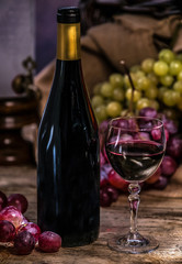 Ripe grapes red wine glass and bottle of wine on a wooden background
