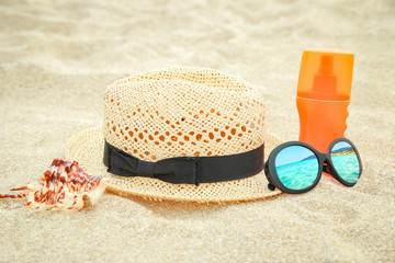 Fototapeta na wymiar beautiful hat with glasses and cream on the sea in the sand background