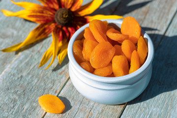 Tasty orange dried apricots in a blue bowl on a wooden background with a flower. Remedy for constipation.
