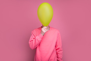 Picture of unknown man stand alone and hide face with green balloon. Isolated over pink background. Incognito person.