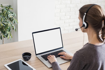 Young woman working at home. Student girl using laptop computer with headset. Online meeting, work,...