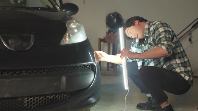 A mechanic inspects a car with a lamp and talking on the phone