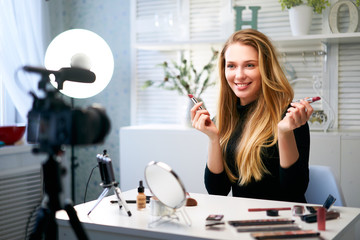 Beauty blogger woman filming daily make-up routine tutorial near camera on tripod. Influencer...