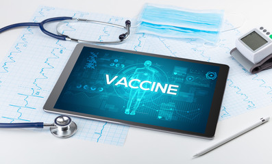 Tablet pc and doctor tools with VACCINE inscription, coronavirus concept