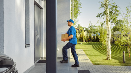 Delivery Man House and Delivers Cardboard Box Package to a Big Beautiful House in the Suburbs. In the Background Cute Suburban Neighbourhood. Side View Shot