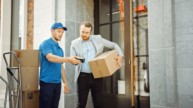 Delivery Man Gives Postal Package to a Business Customer, Who Signs Electronic Signature POD Device. In Stylish Modern Urban Office Area Courier Delivers Cardboard Box Parcel to a Man