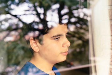 Kid looking out the window at the street waiting for the end of the confinement due to the global pandemic by the virus COVID-19