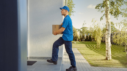 Delivery Man Holding Card Board Package Walks to the House. Delivering Postal Parcel. In the...