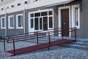 Wheelchair access ramp for entrance of residential multistory building, city street and tiles sidewalk