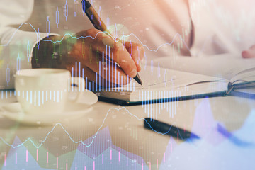 Double exposure of man's hands writing notes of stock market with forex chart.