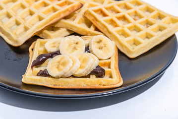 Belgian homemade waffles with chocolate sauce and bananas on a black plate