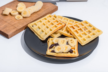 Belgian homemade waffles with chocolate sauce and bananas on a black plate