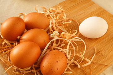 One white chicken egg against a group of brown eggs on the table