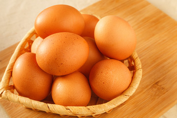 Raw organic brown chicken eggs in wicker basket on kitchen wooden table