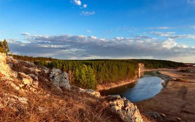 Fototapeta na wymiar spring landscape. view from the cliff to the river enveloping the coniferous forest. beautiful blue sky and clouds