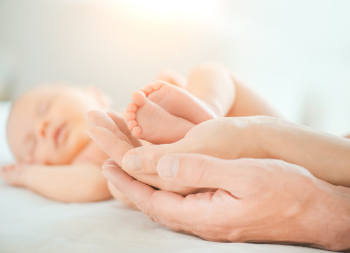 Baby feet in mother and father hands. Tiny Newborn Baby's feet on hands closeup. Mom, Dad and Child together. Healthy and Happy Family concept. Parents. Beautiful photo of Parenthood, adoption 