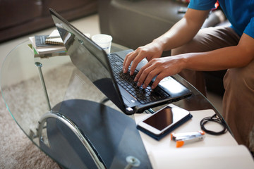 Asian man using a living room as home office while typing a computer laptop keyboard to contact colleague about job details and recently situation of company clients.