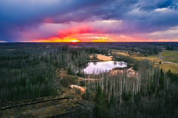 Aerial view over forest with dark storm clouds. Lake in the forest at colorful twilight. 
