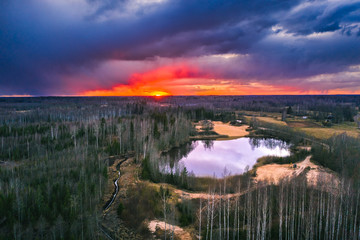 Aerial view over forest with dark storm clouds. Lake in the forest at colorful twilight. 
