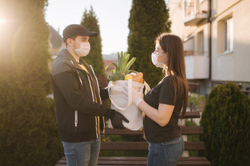 Courier in protective mask and medical gloves delivers fresh food for female customer. Delivery service under quarantine. Coronavirus covid-19 theme