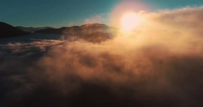 Moving orange clouds blue sky scenic aerial view. Drone flies high back in blue sky through the fluffy clouds in the evening at the bright sun. Sun is hidden behind the clouds at sunset the fog