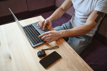 Unrecognizable man hands with smartphone and headphones working on a laptop during coronavirus...
