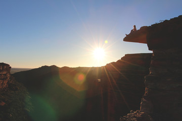 Person sitting on the edge of a cliff watching the sunset