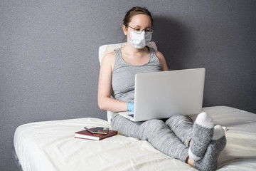 A girl works at a laptop in her bed during an epidemic.