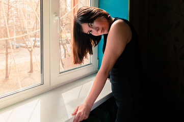young beautiful brunette girl in a black dress leaned on a windowsill near a barred window