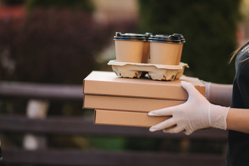 Naklejka premium Closeup of courier give order to customer. Man from delivery service bring pizza and coffee. Hands in protective mask