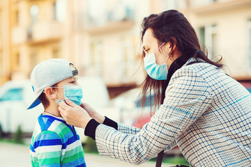 Mother puts her son a face protective mask outdoors. Stop the coronavirus spreading. Protective measures.