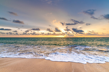 Beautiful sunset above sea or ocean. Vibrant and soft colors, magic light. Small clouds on the sky, reflection of sun in the water and sand on beach. Concept of romantic time on vacation in tropical.
