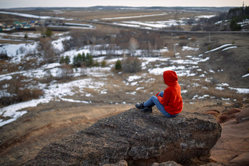 Beautiful girl looks at the sunset from a high mountain in the spring evening.