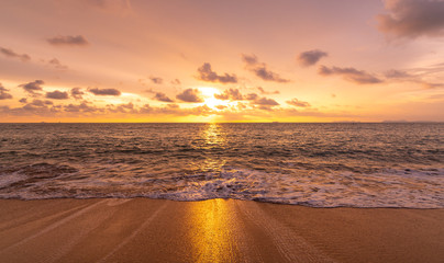 Beautiful sunset above sea or ocean. Vibrant and soft colors, magic light. Small clouds on the sky, reflection of sun in the water and sand on beach. Concept of romantic time on vacation in tropical.