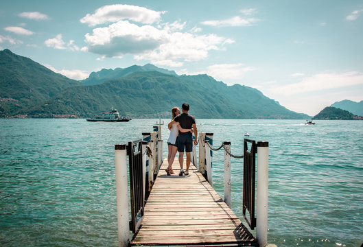 Junges Paar am Steg genießt Arm in Arm die Aussicht am Comer See in Italien