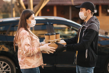 Young woman in protective mask and medical mask take order from delivery boy outside. Food delivery in quarantine. Courier bring Pizza and coffee for customer