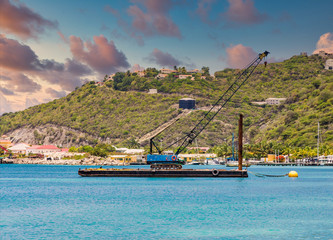 A blue crane on a working barge over blue water in the harbor of Philipsburg in St Martin