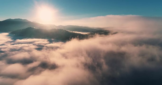 Flying over the clouds during morning sunrise in Carpathian Mountains, Ukraine.golden fluffy clouds moving softly on the sky and the sun shining through the clouds with beautiful rays and lens flare. 