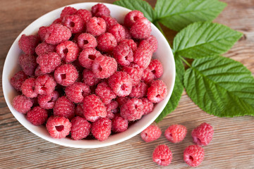 Fresh raspberries in a plate on a rustic wooden background, top view