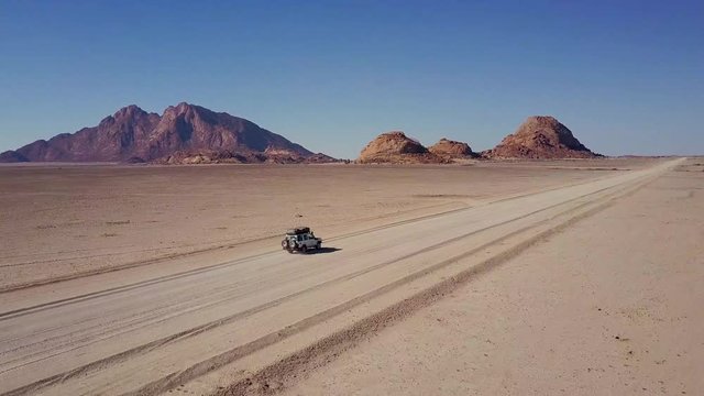 Aerial shot of a 4x4 car driving through the empty desert landscape towards Spitzoppe in Namibia.