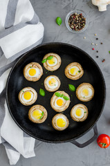 Baked stuffed mushrooms with quail eggs with thyme leaves and basilin in an old cast-iron frying pan on a dark concrete background. Easter appetizer. Vertical orientation. Top view.