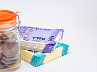 A coin filled glass jar defocused with money notes behind, shot on white background for saving concept.