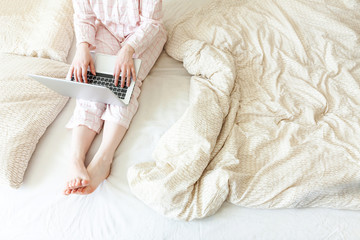 Mobile Office at home. Young woman in pajamas sitting on bed at home working using on laptop pc computer. Lifestyle girl studying indoors. Freelance business quarantine concept.