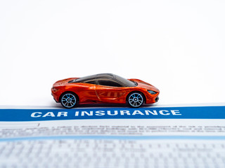 High angle close up shot of an orange sports car toy with insurance paper on white background.