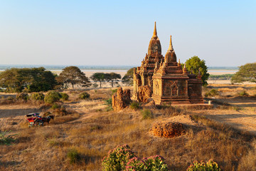 Myanmar pagoda near the green trees and yellow grass. Horse cab near the ancient temple.